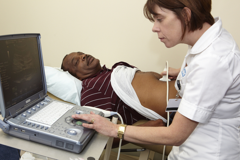 A white female clinician conducts na ultrasound on the abdoman of an older black man.